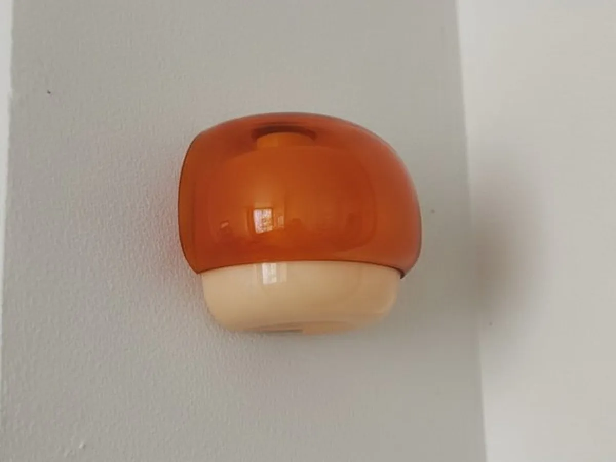 Orange Clinco lamp fully visible on a white wall, photographed by Beriol G.