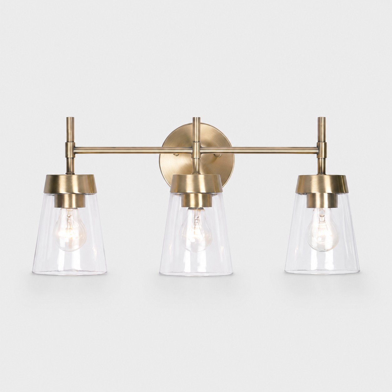 Brushed brass three-light vanity wall fixture on a light studio background