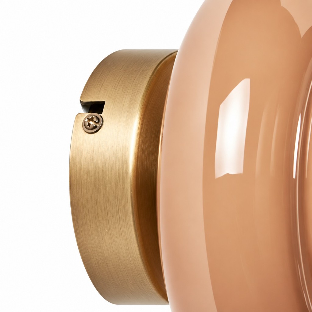 Close-up of brushed brass wall disc and recessed screw next to pale glass
