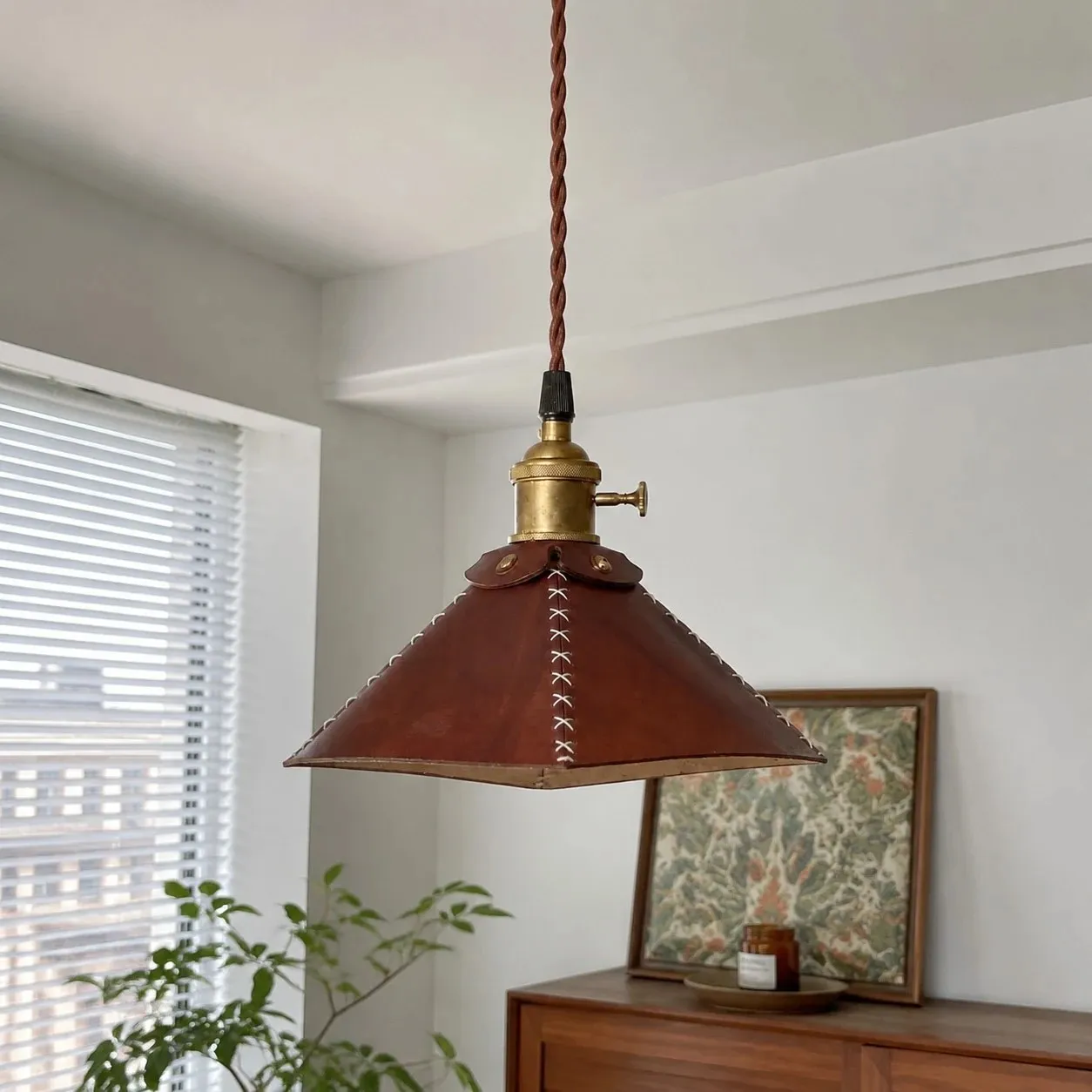 Leather pyramid pendant lamp above a sideboard by the window