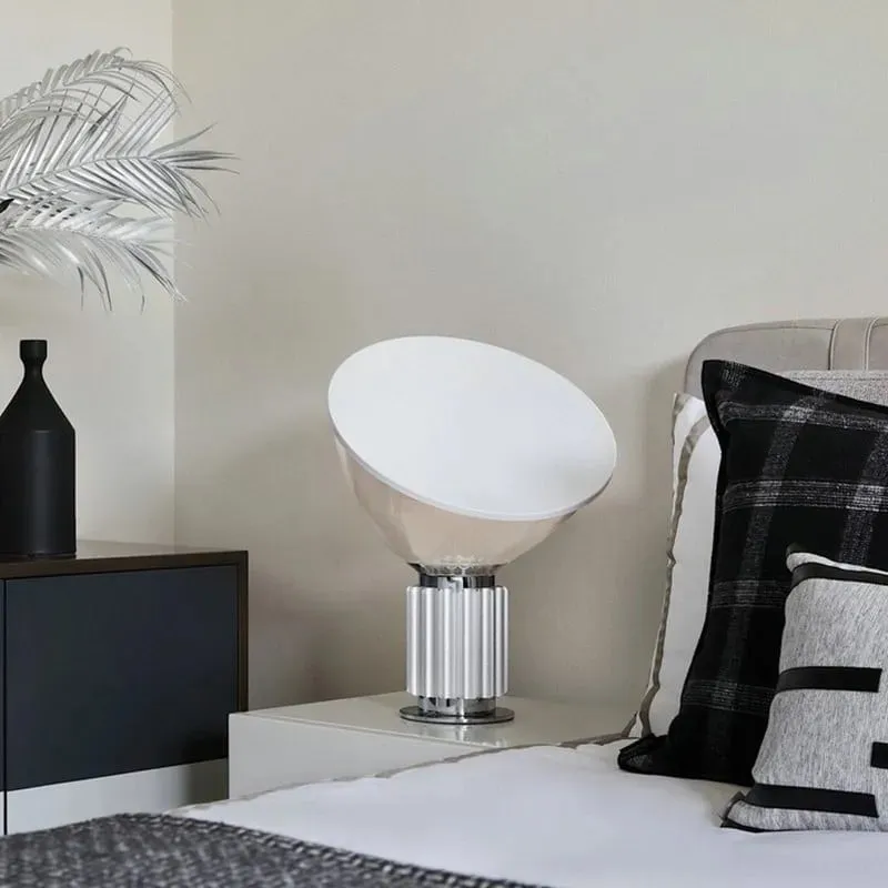 Lampe en bol argenté sur une table de chevet près d’un lit